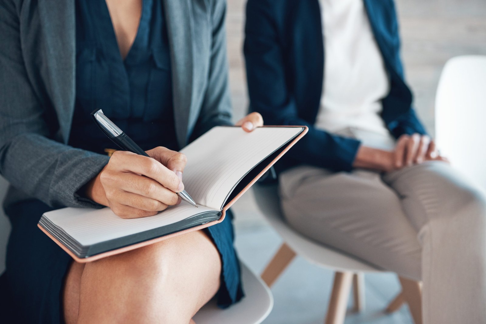 Woman, notebook and writing at job interview for notes, waiting room and candidates for opportunity. Female person, schedule and diary for appointments, company and planning in journal with coworkers.